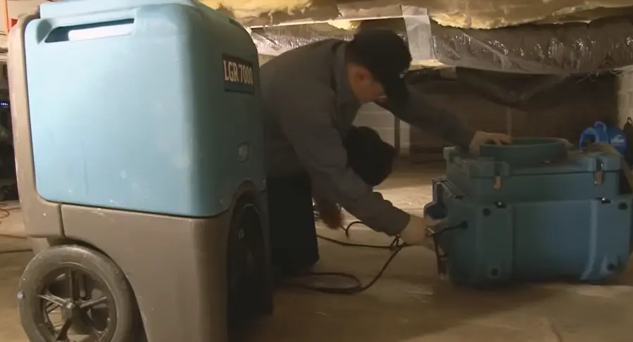 Flood damage cleanup Garland TX: technician setting up a dehumidifier and air mover in a crawlspace to dry the structure