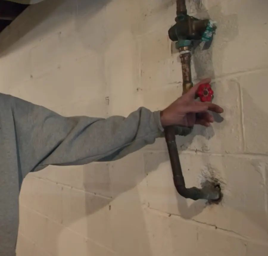 Hand turning a main water shutoff valve after a burst pipe
