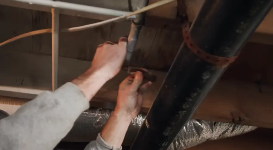 Hands working on a pipe joint under the floor joists